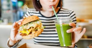 Woman's jaw popping after holding burger and drinking green juice.