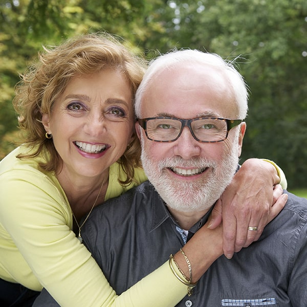 Mature couple smiling and hugging in a garden after their dental implant treatment